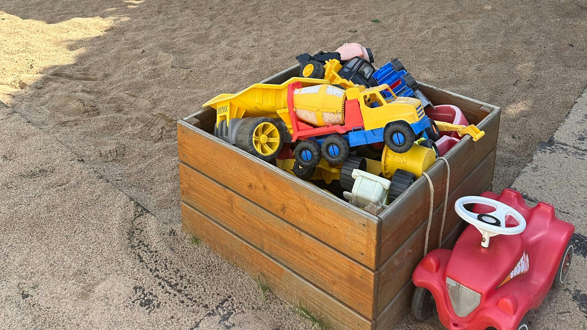 Eine viereckige Kiste aus Holz ist gefüllt mit Spielzeug für den Sandkasten.