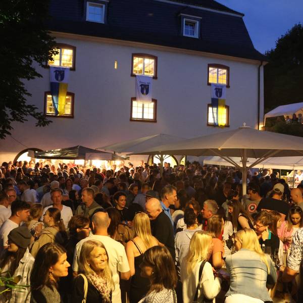 Eine große Menschenmenge in der Dämmerung vor dem Burghaus.