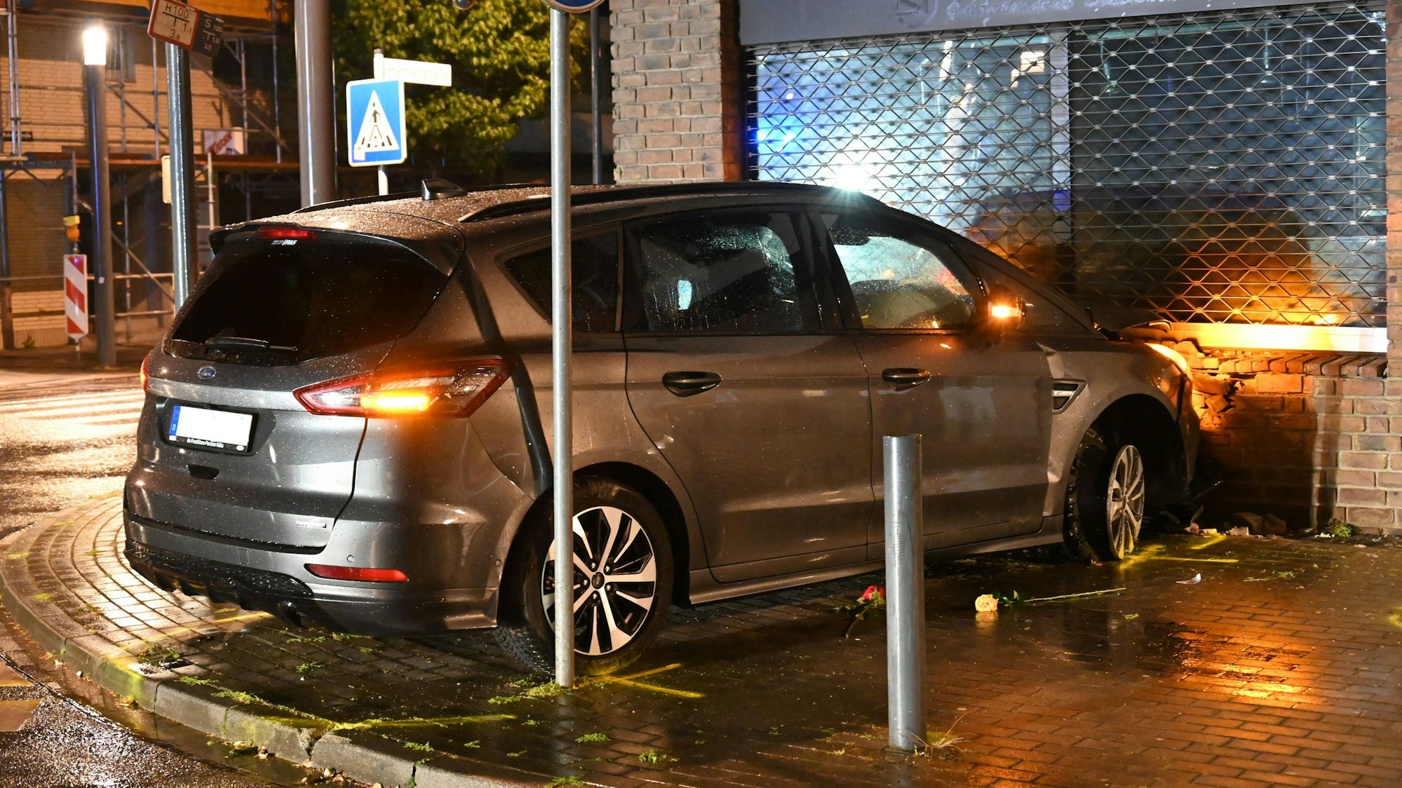 Ein dunkelgraues Auto der Marke Ford steht unmittelbar vor einer Hauswand, die beschädigt ist.