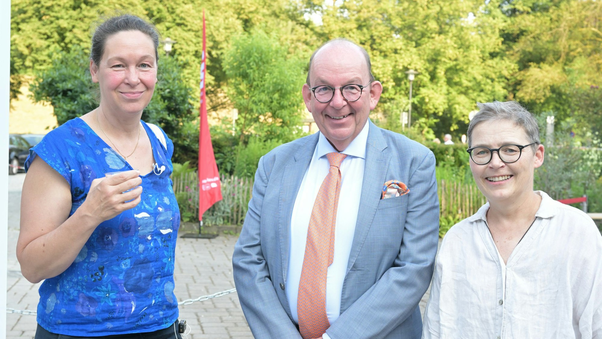 Zwei Frauen und ein Mann stehen in einem Garten.