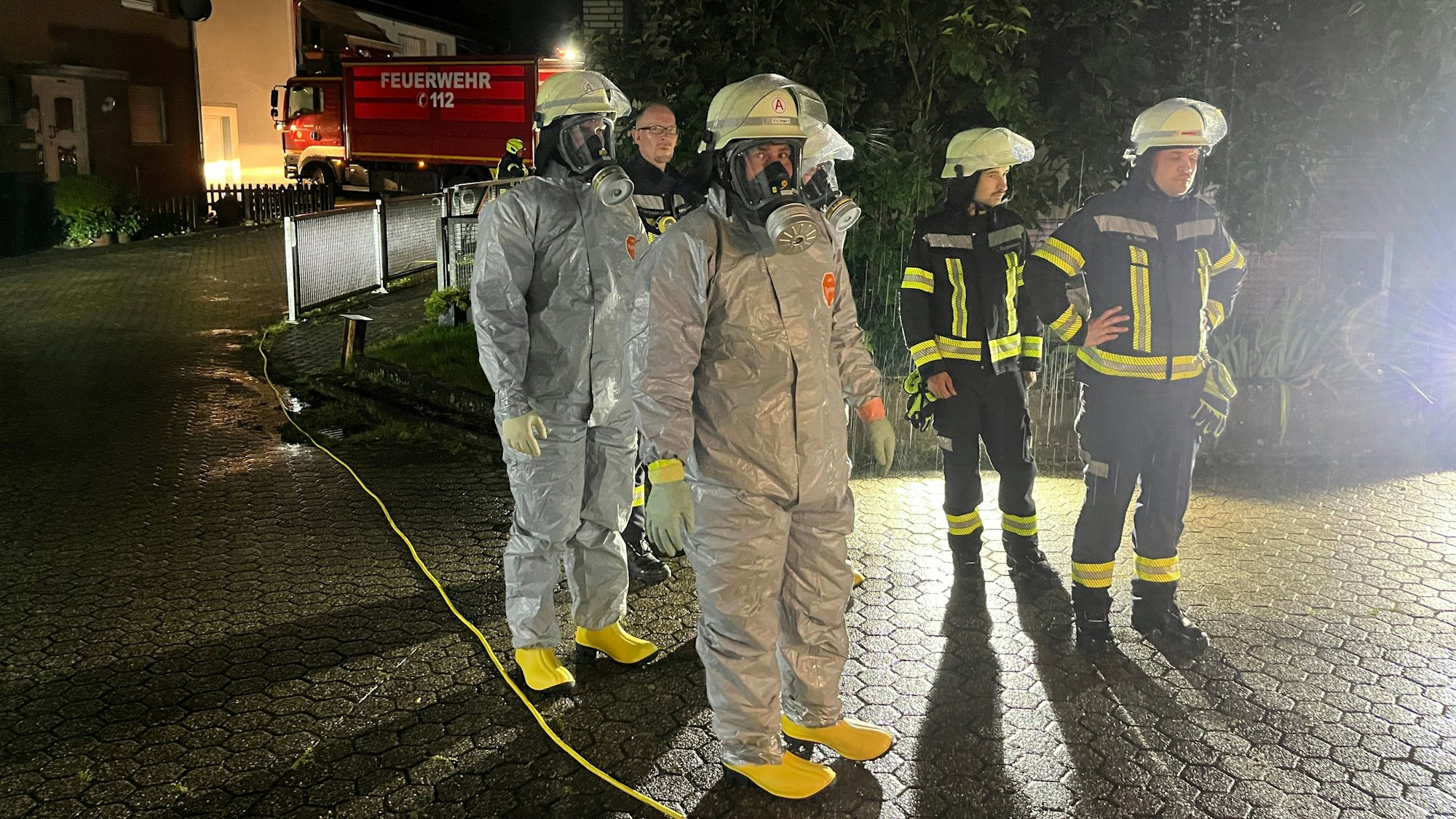 Einsatzkräfte in weißen Einmalanzügen stehen auf einem Hof.