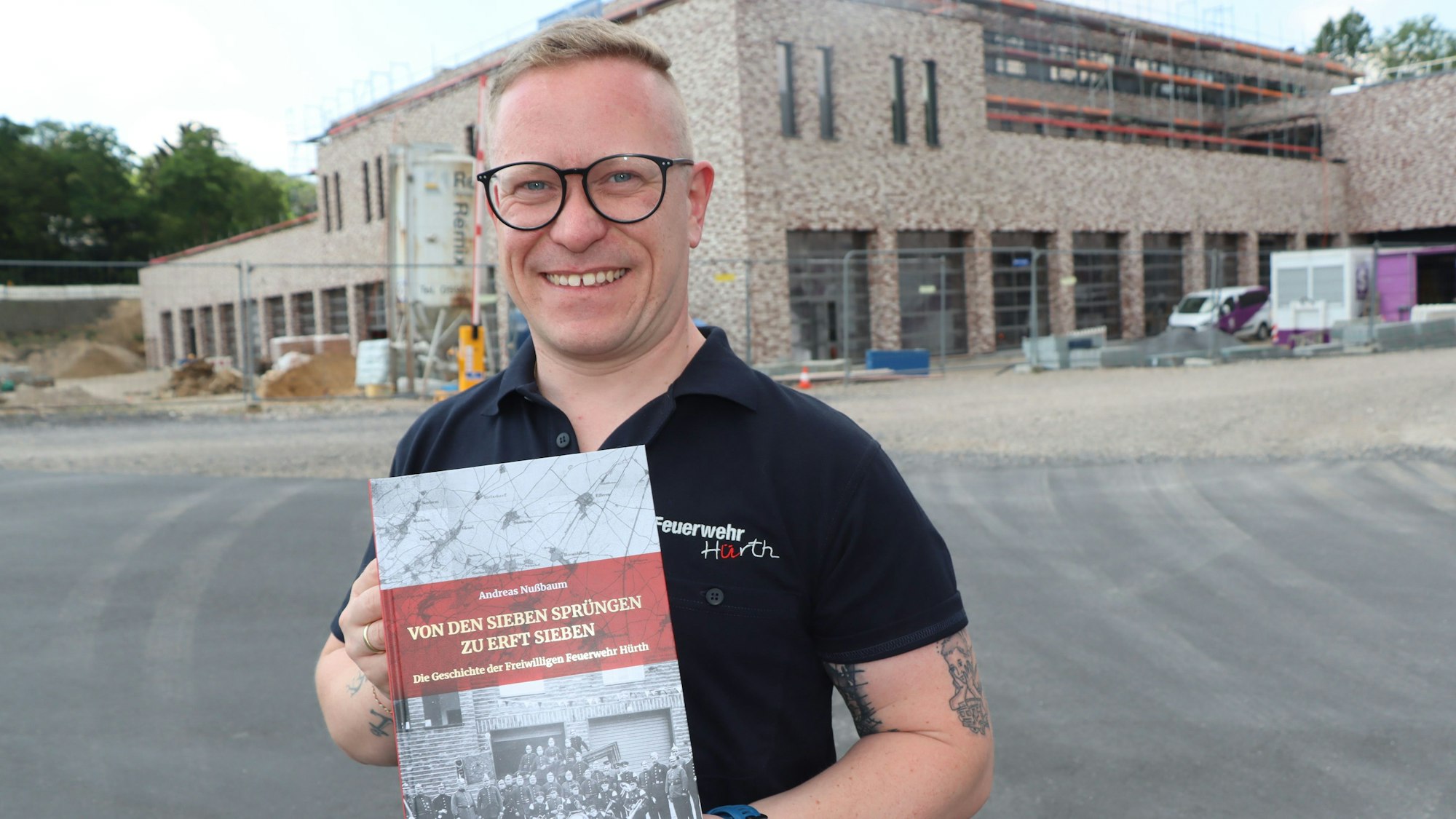 Ein Mann im Poloshirt mit dem Logo der Feuerwehr Hürth zeigt sein Buch über die Geschichte der Hürther Feuerwehr.