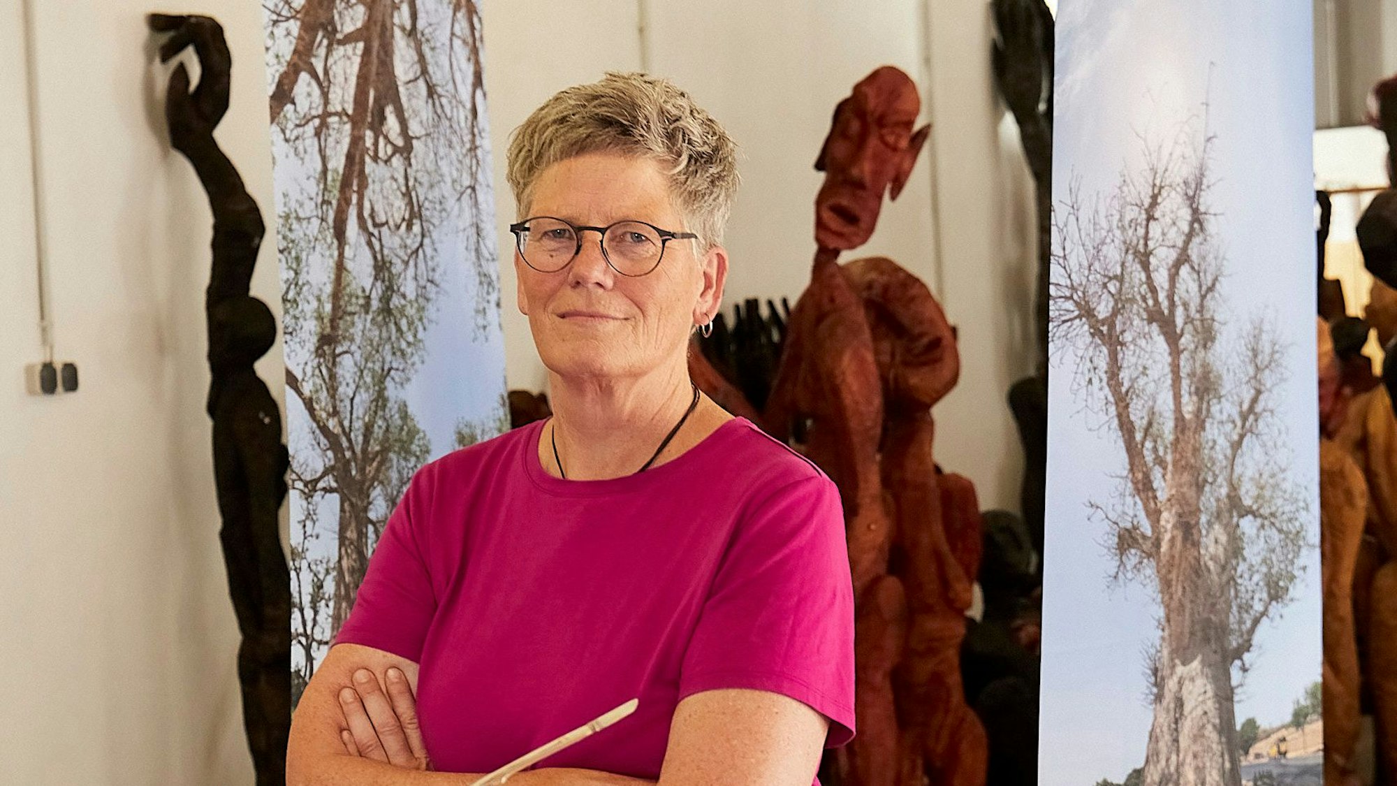 Die Künstlerin Rendel Freude steht inmitten von Skulpturen und Fotofahnen.