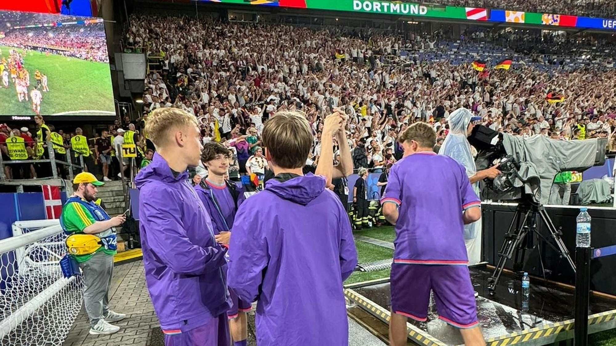 Julian Seliger aus Kirspenich war beim EM-Spiel Deutschland gegen Dänemark als Balljunge dabei. Auf dem Bild ist er links mit drei anderen Balljungen in lila Shirts vor den vollen Rängen des Stadions in Dortmund zu sehen.