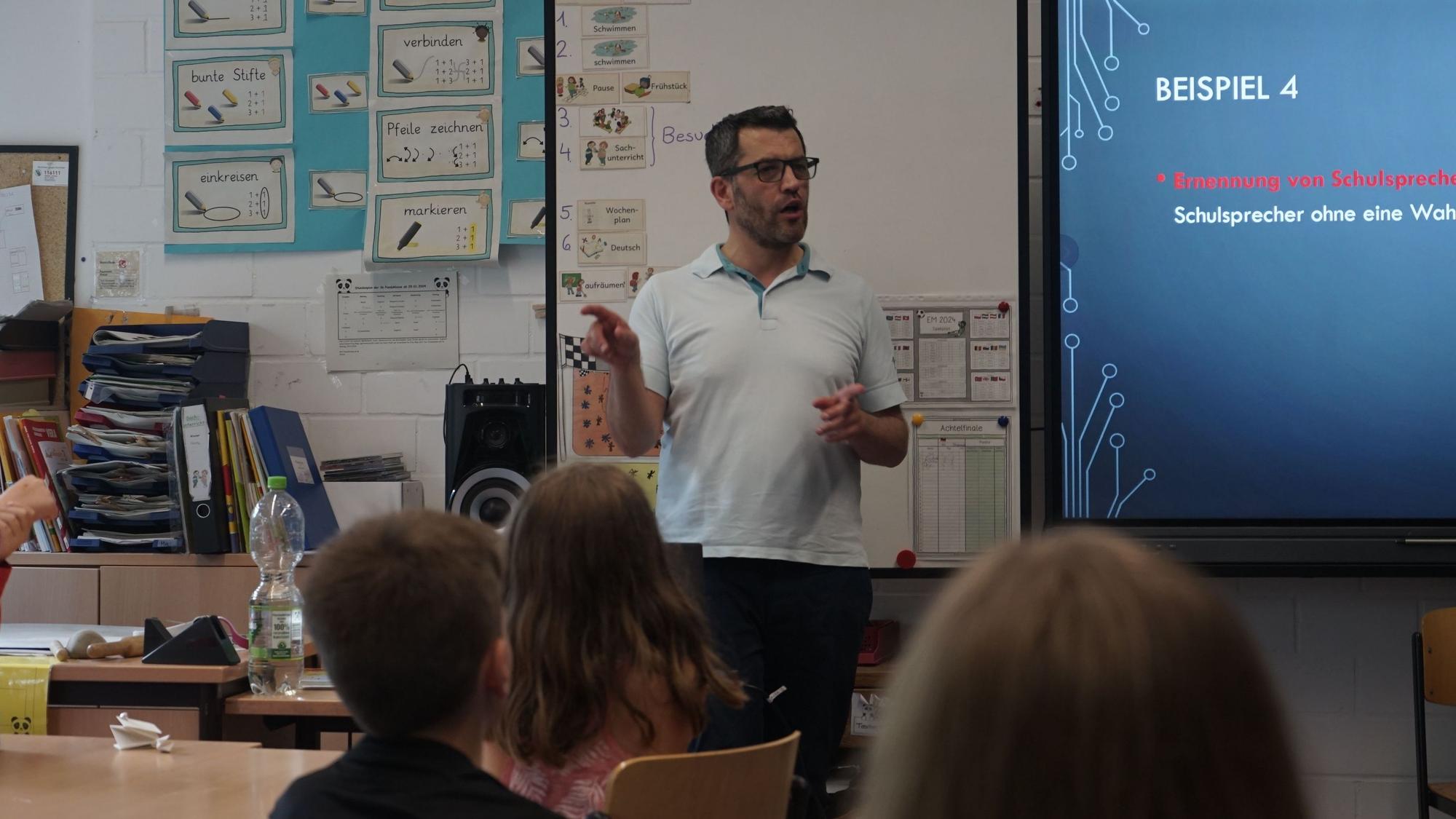 Ahmet Özdemir steht vor der Tafel in einem Klassenraum. Kinder blicken in seine Richtung.