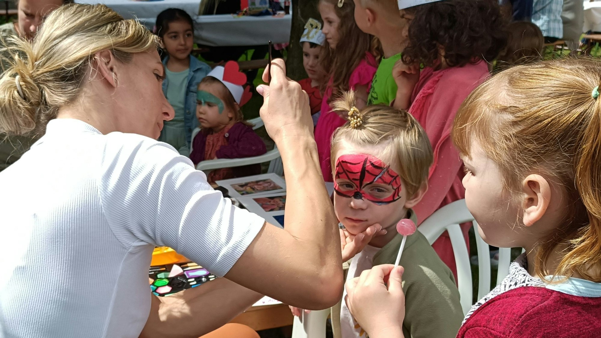 Eine Frau schminkt Kinder mit bunten Farben.