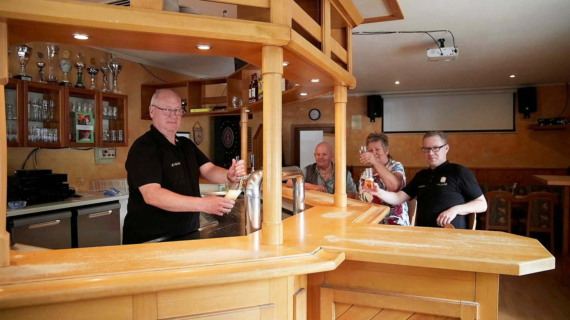 Oliver Peters, der Vorsitzende des Kneipenvereins in Hellenthal-Wolfert, steht an der Theke und zapft ein Bier. Im Hintergrund sitzen drei Gäste.