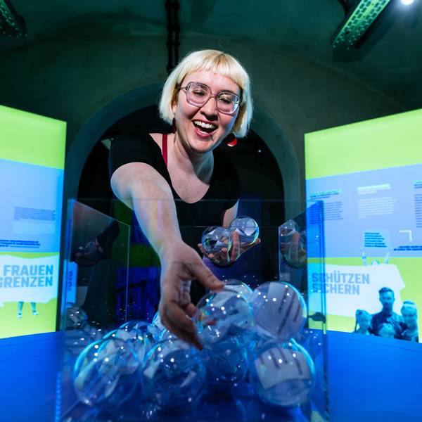 Kuratorin Rebekka Blum greift in eine Vase mit durchsichtigen Kugeln in denen Zettel sind.