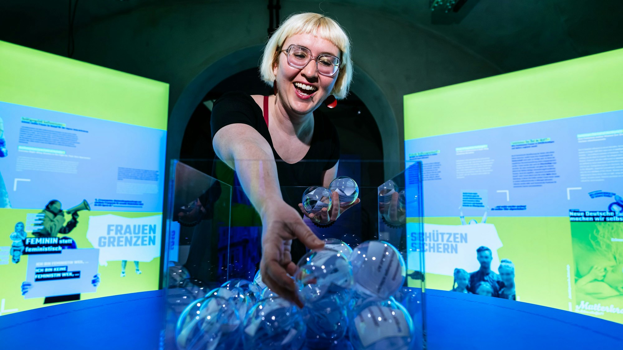 Kuratorin Rebekka Blum greift in eine Vase mit durchsichtigen Kugeln in denen Zettel sind.