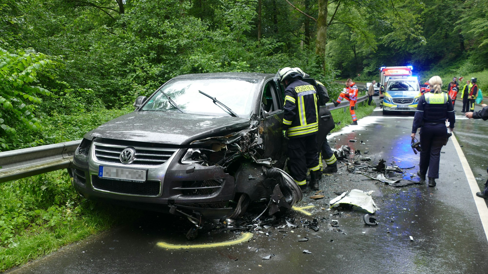 Feuerwehrleute stehen um ein beschädigtes Auto herum.