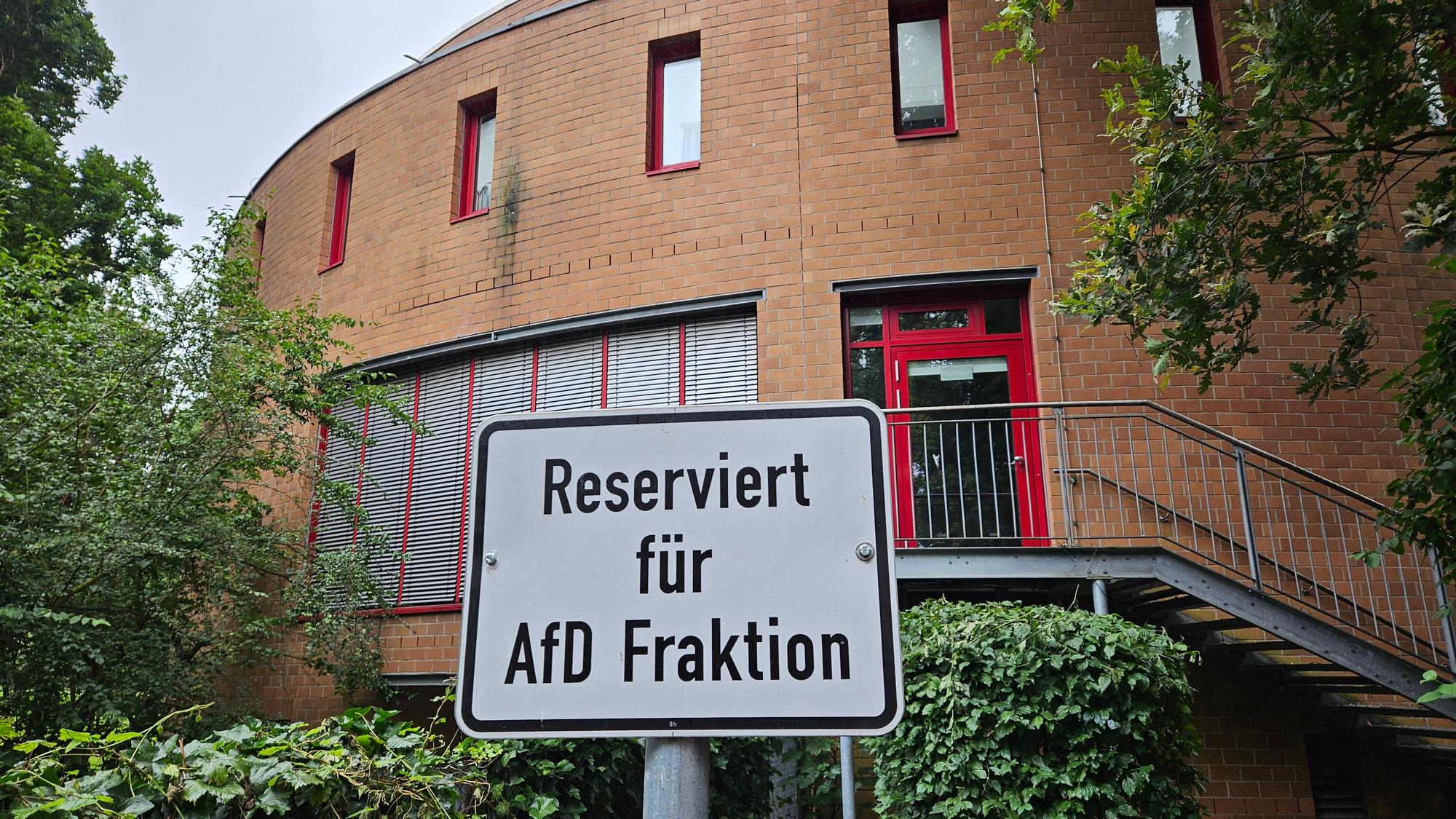 Auf dem Foto ist ein Gebäude im Hintergrund zu sehen, das Kreishaus in Bergheim. Davor steht ein Schild an einem Parkplatz mit dem Text „Reserviert für AfD-Fraktion“.