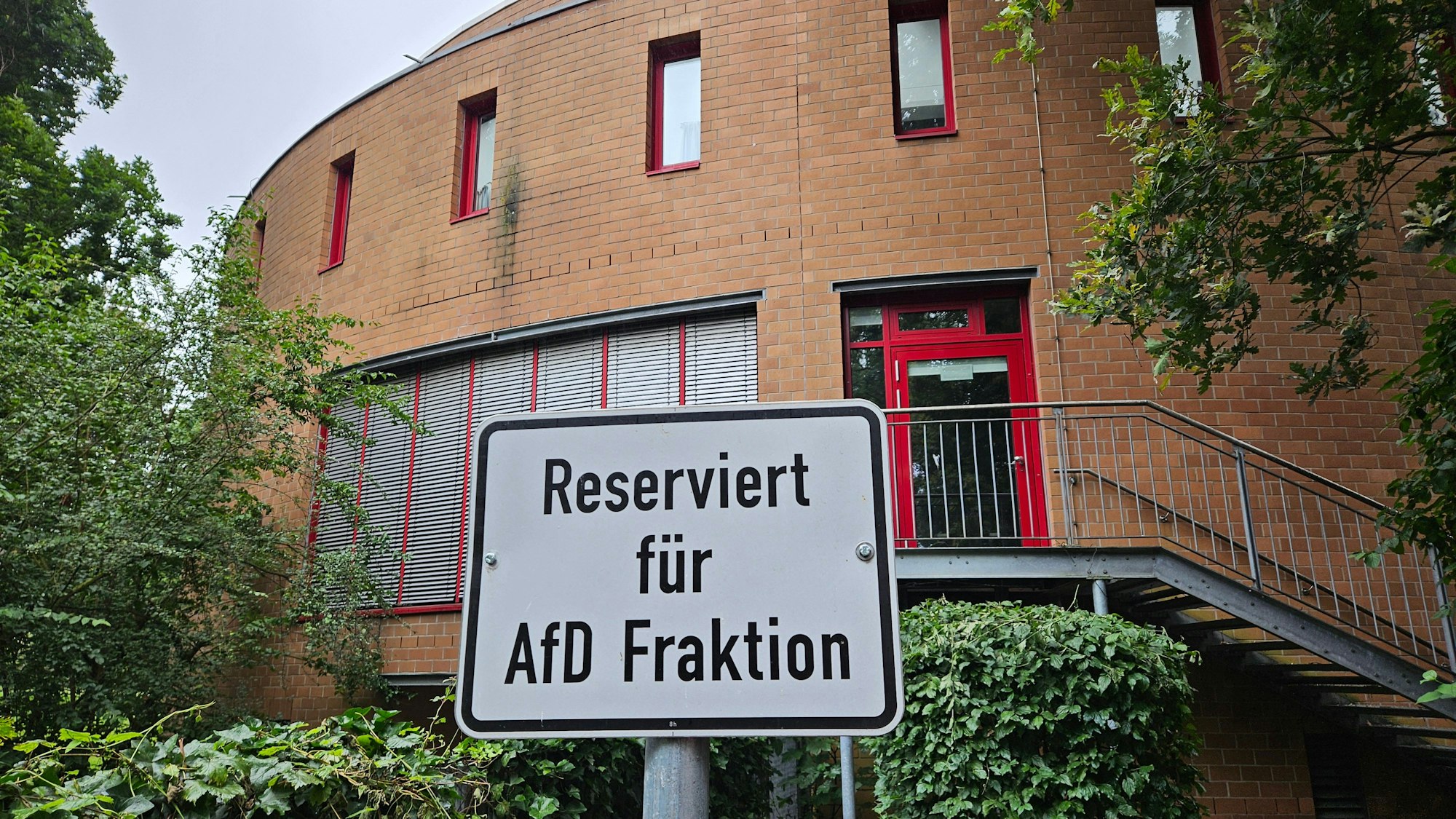 Auf dem Foto ist ein Gebäude im Hintergrund zu sehen, das Kreishaus in Bergheim. Davor steht ein Schild an einem Parkplatz mit dem Text „Reserviert für AfD-Fraktion“.