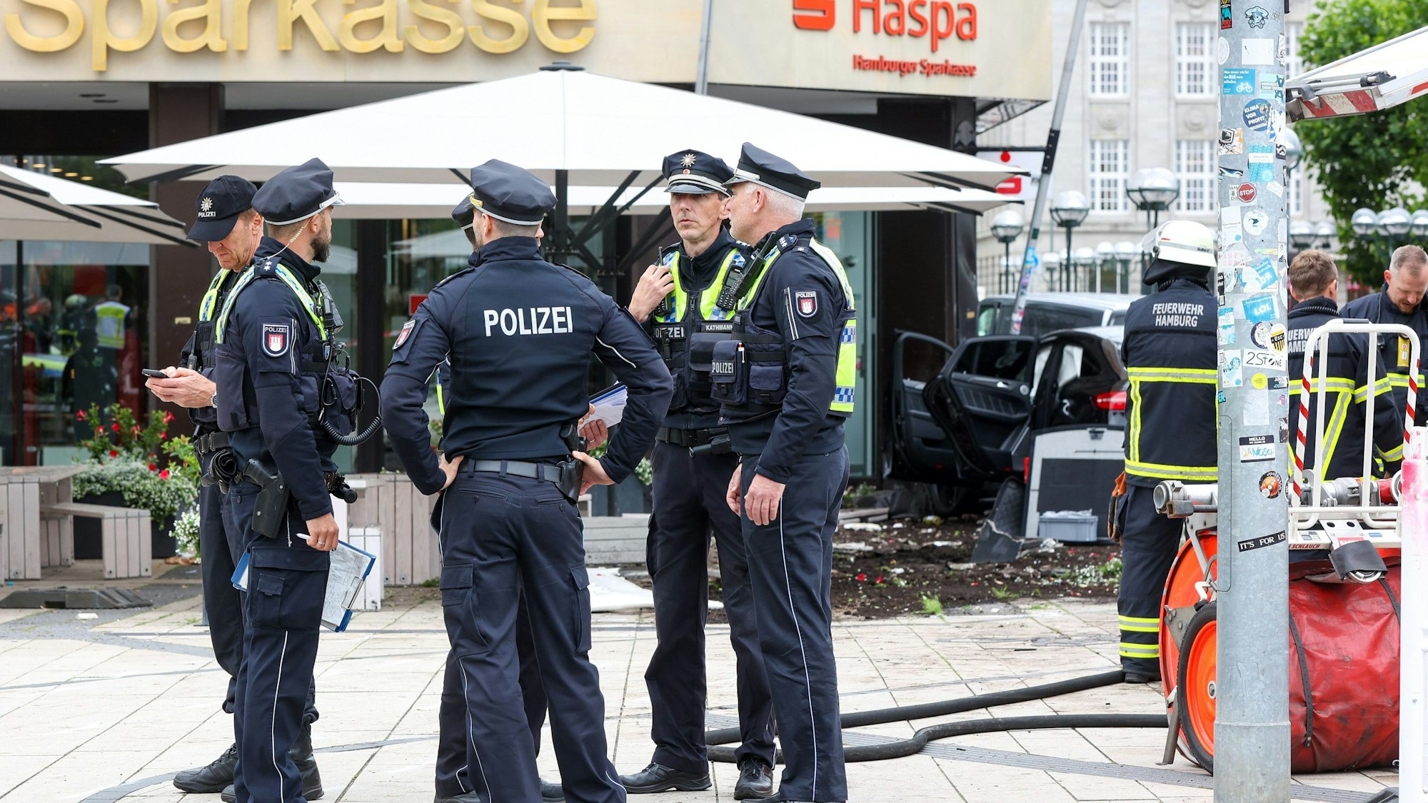 02.07.2024, Hamburg: Einsatzkräfte stehen vor einer Sparkasse in der Hamburger Innenstadt, in der ein Auto gefahren ist.