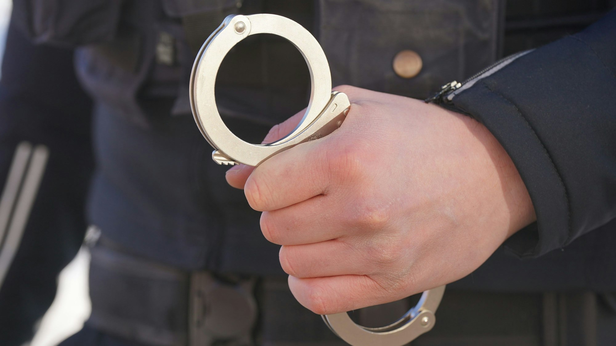Das Symbolbild (Detailaufnahme) zeigt die Hand eines Polizisten, der eine Handfessel festhält.