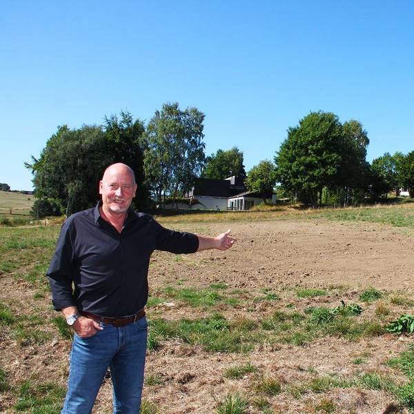 Ein Mann in Jeans und schwarzem Hemd zeigt auf eine Wiese, auf der künftig Häuser gebaut werden sollen. Im Hintergrund sind bereits Häuser zu sehen.