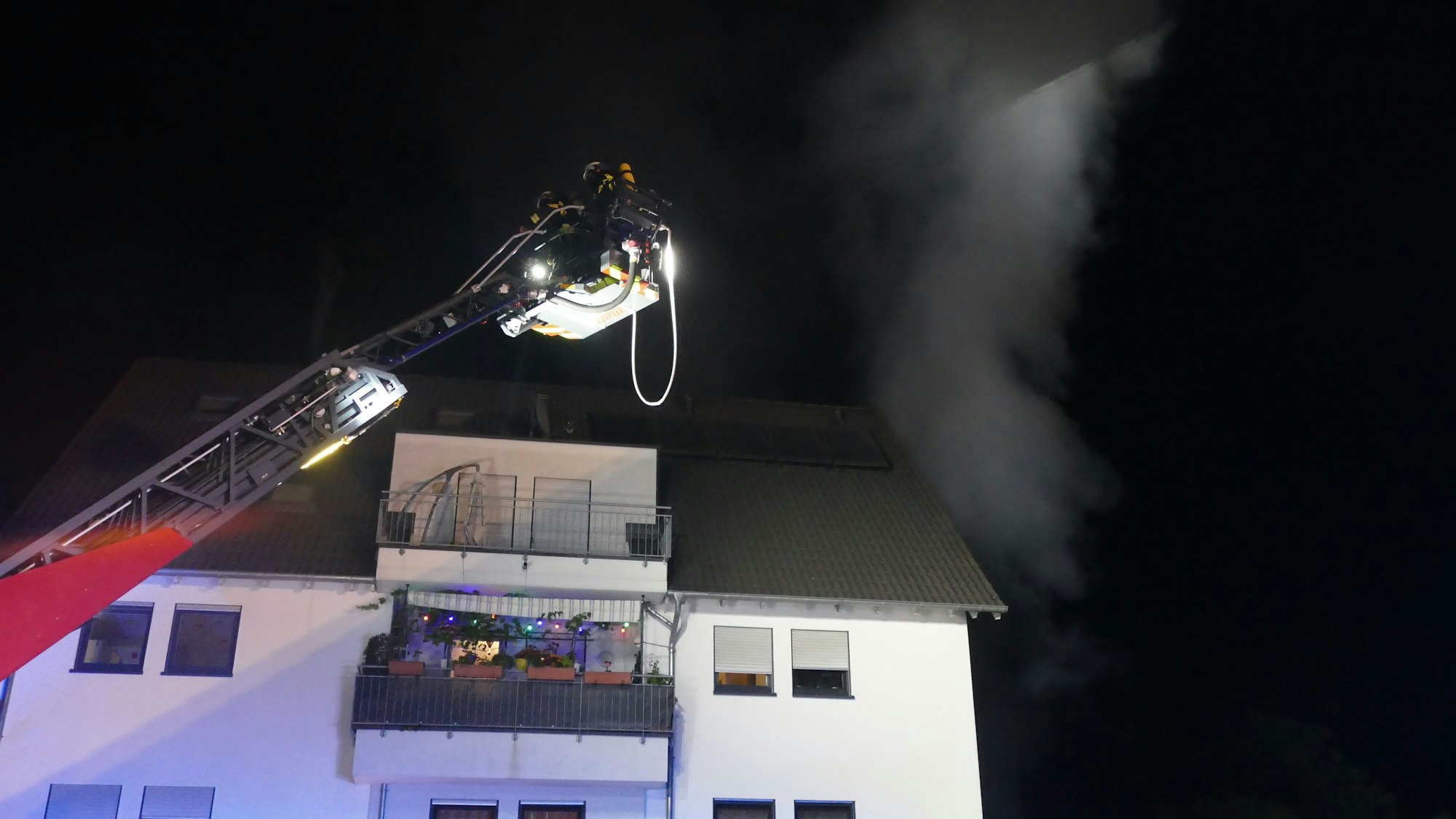 Eine Drehleiter der Feuerwehr steht über einem Haus, aus dem Rauch kommt.