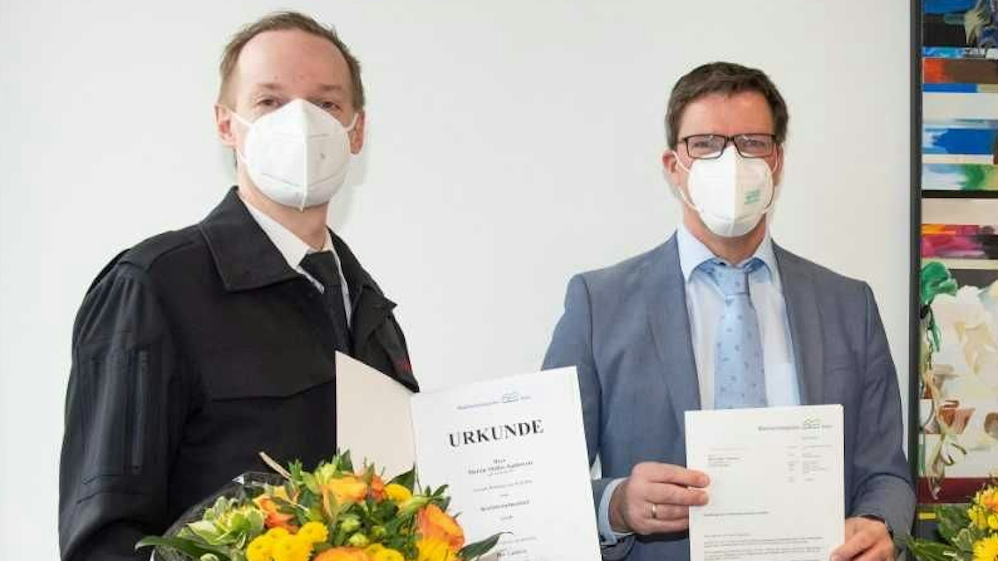 Zwei Männer stehen mit Mund-Nase-Schutz und Urkunden im Kreishaus.