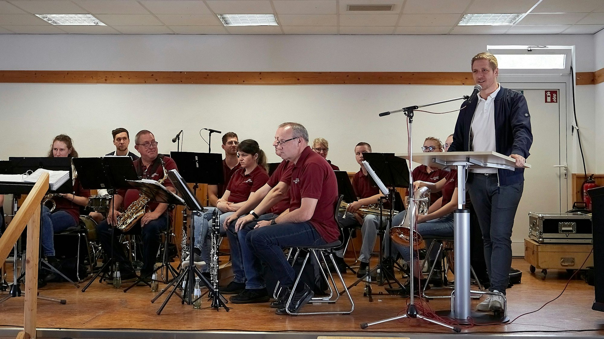 Der Euskirchener Landrat Markus Ramers steht rechts an einem Pult und spricht in ein Mikrofon. Daneben sitzen Musiker des Musikvereins Wolfert.