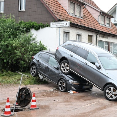 Auf einer Straße in Miedelsbach in Baden-Württemberg stehen Fahrzeuge, die durch ein Hochwasser nach einem Unwetter weggespült wurden.