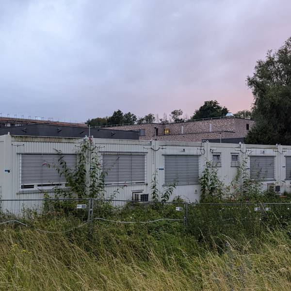 Das Foto zeigt Baucontainer auf einem verwilderten Grundstück vor der Baustelle der Feuerwache in Hermülheim.