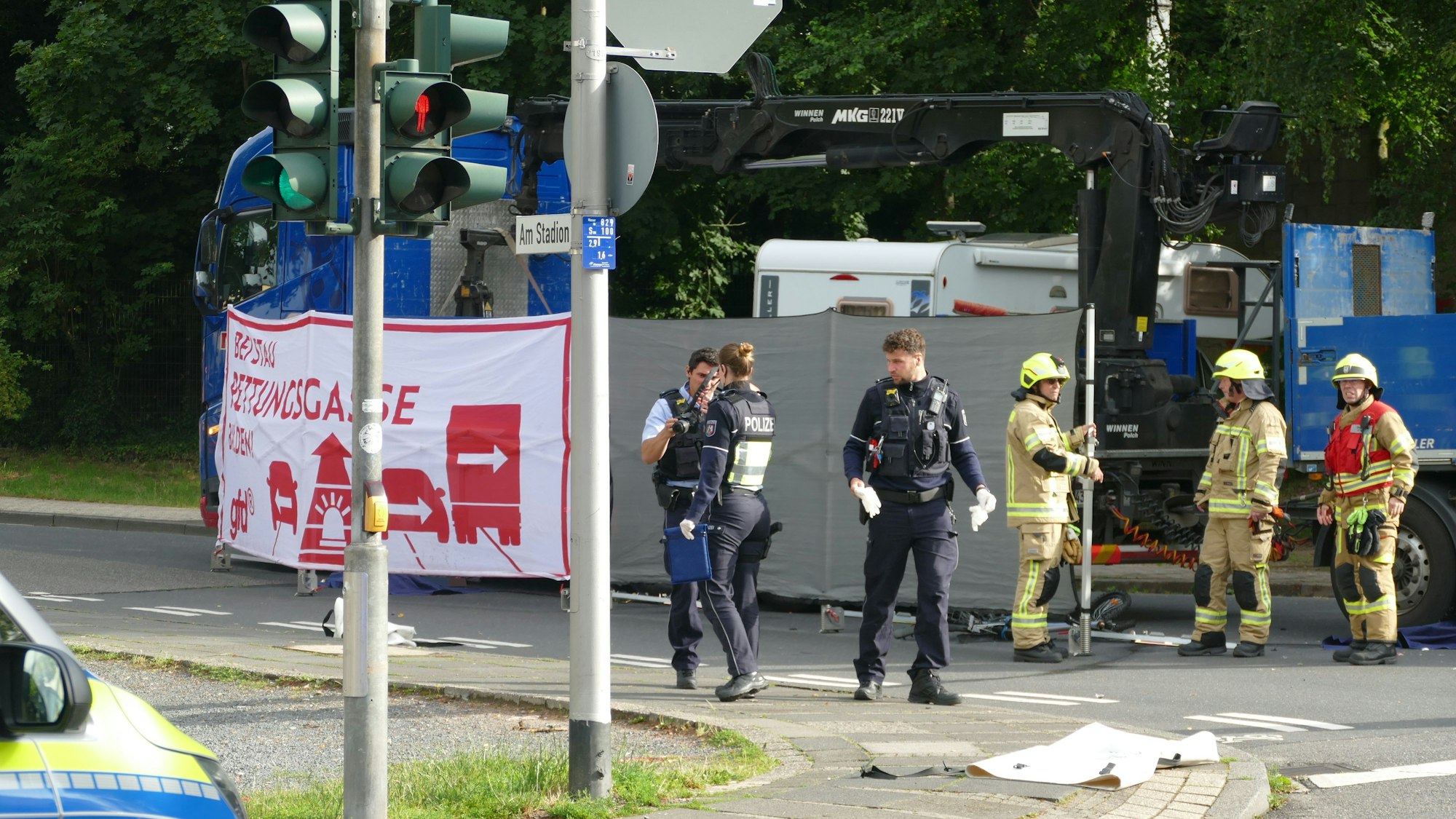 Polizisten und Feuerwehrleute stehen vor einem Lastwagen, vor dem ein Sichtschutz aufgebaut ist.
