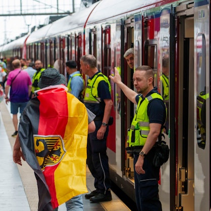 23.06.2024, Hessen, Frankfurt/Main: Fußball, UEFA Euro 2024, EM, Schweiz - Deutschland, Vorrunde, Gruppe A, Spieltag 3, Frankfurt Arena, Sicherheitspersonal der Bahn weisst einem deutschen Fan den Weg zu einem freien Abteil, ganz am Ende des Zuges. Fussballfans die mit dem Zug ab Hauptbahnhof zum Deutsche Bank Park, dem Austragungsort der Begegnung Schweiz - Deutschland, kommen wollen, werden hart geprüft. Die Menschen müssen in völlig überfüllten und verspäteten Zügen bei hohen Temperaturen ausharren. Foto: Andreas Arnold/dpa +++ dpa-Bildfunk +++