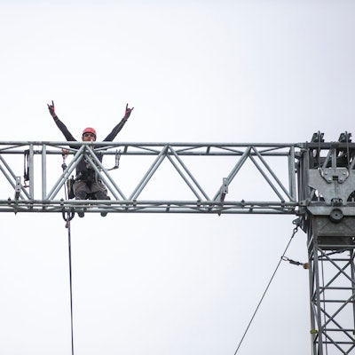 Ein Mann hebt auf einem Gerüst in der Höhe seine Arme.