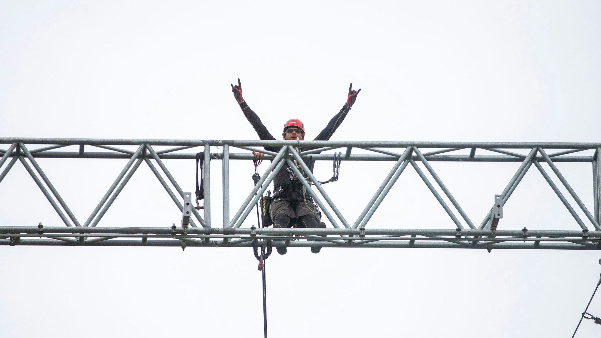 Ein Mann hebt auf einem Gerüst in der Höhe seine Arme.