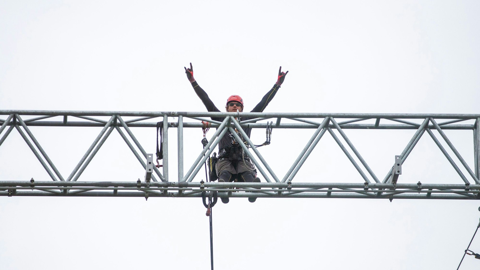 Ein Mann hebt auf einem Gerüst in der Höhe seine Arme.