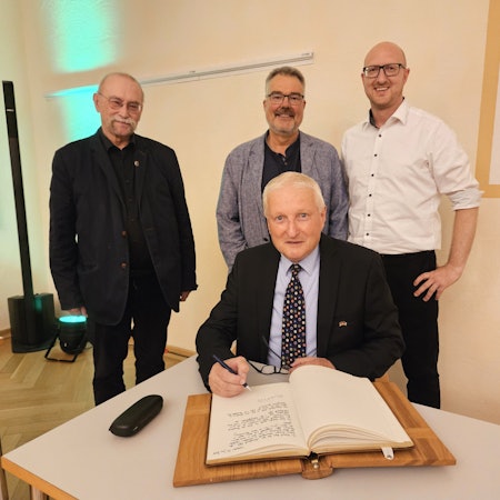 Dr. Michael Röös trägt sich ins Goldene Buch der Stadt Schleiden ein, dahinter stehen Philipp Cuck, Erik Schumacher und Ingo Pfennings.
