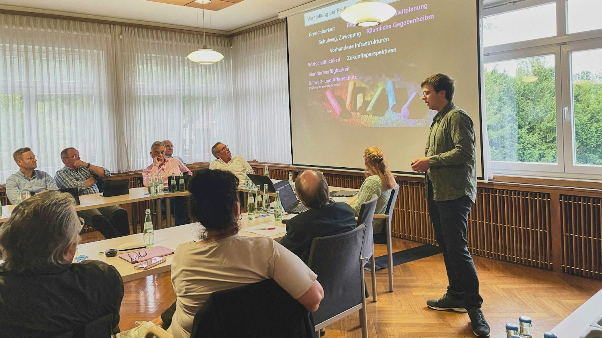 Christian Schmitz vom Planungsbüro PE Becker steht vor einer Leinwand. Hellenthaler Politiker sitzen an Tischen und hören seinem Vortrag zu.