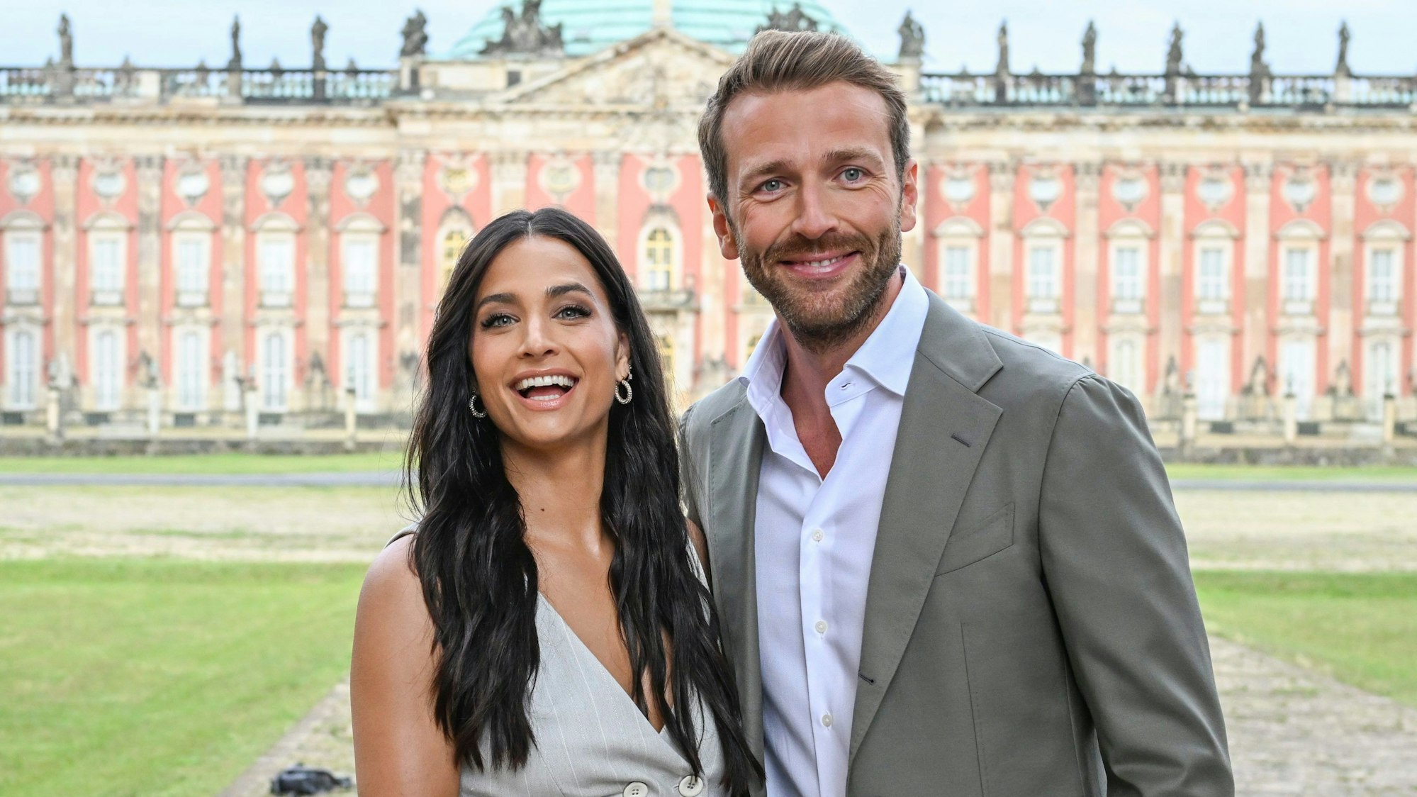 Amira Pocher und Christian Düren lachen vor den Kolonnaden mit Triumphtor am Neuen Palais.