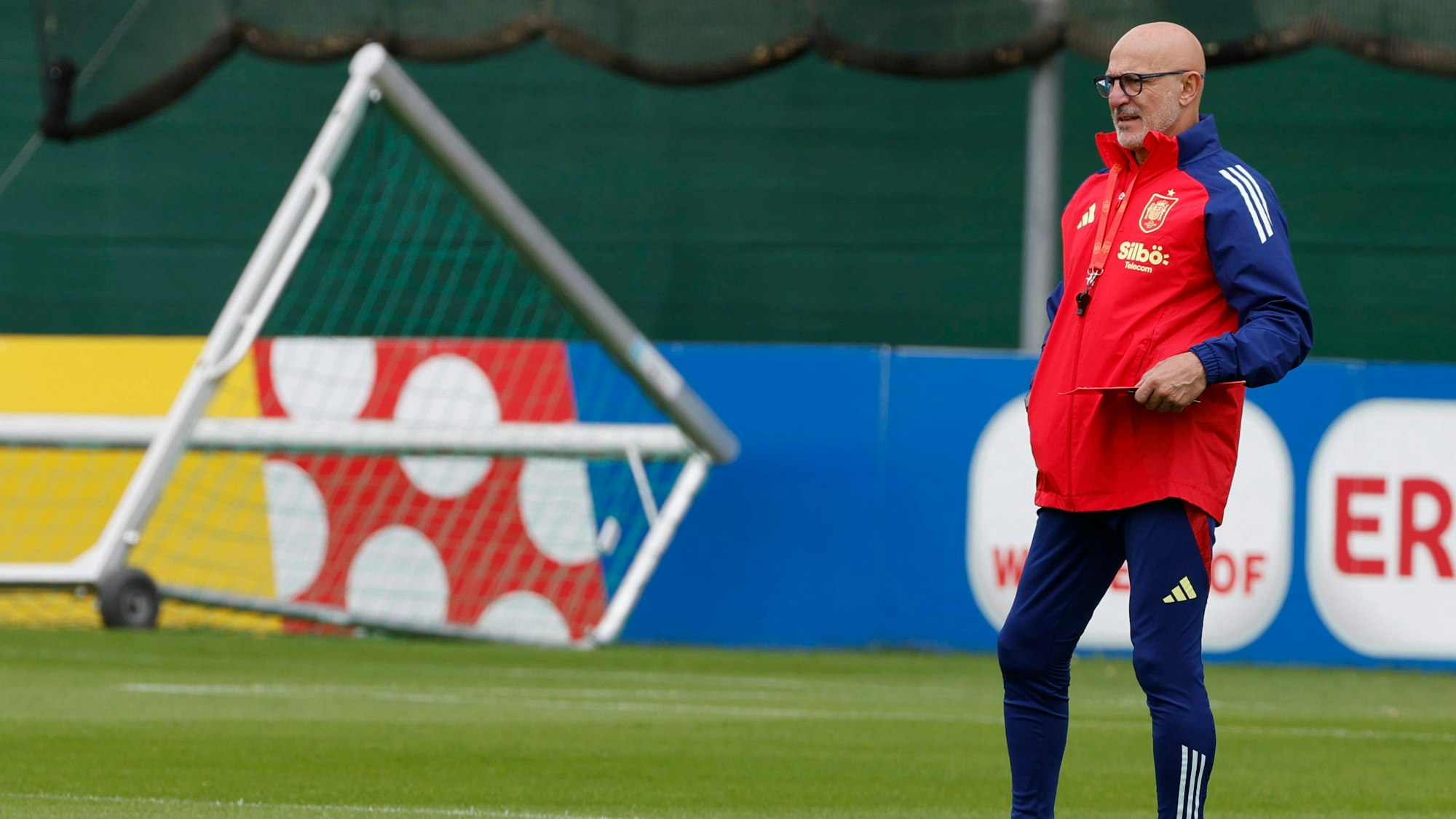 Luis de la Fuente steht in wetterfester rot-blauer Trainingsbekleidung auf dem gepflegten Grün