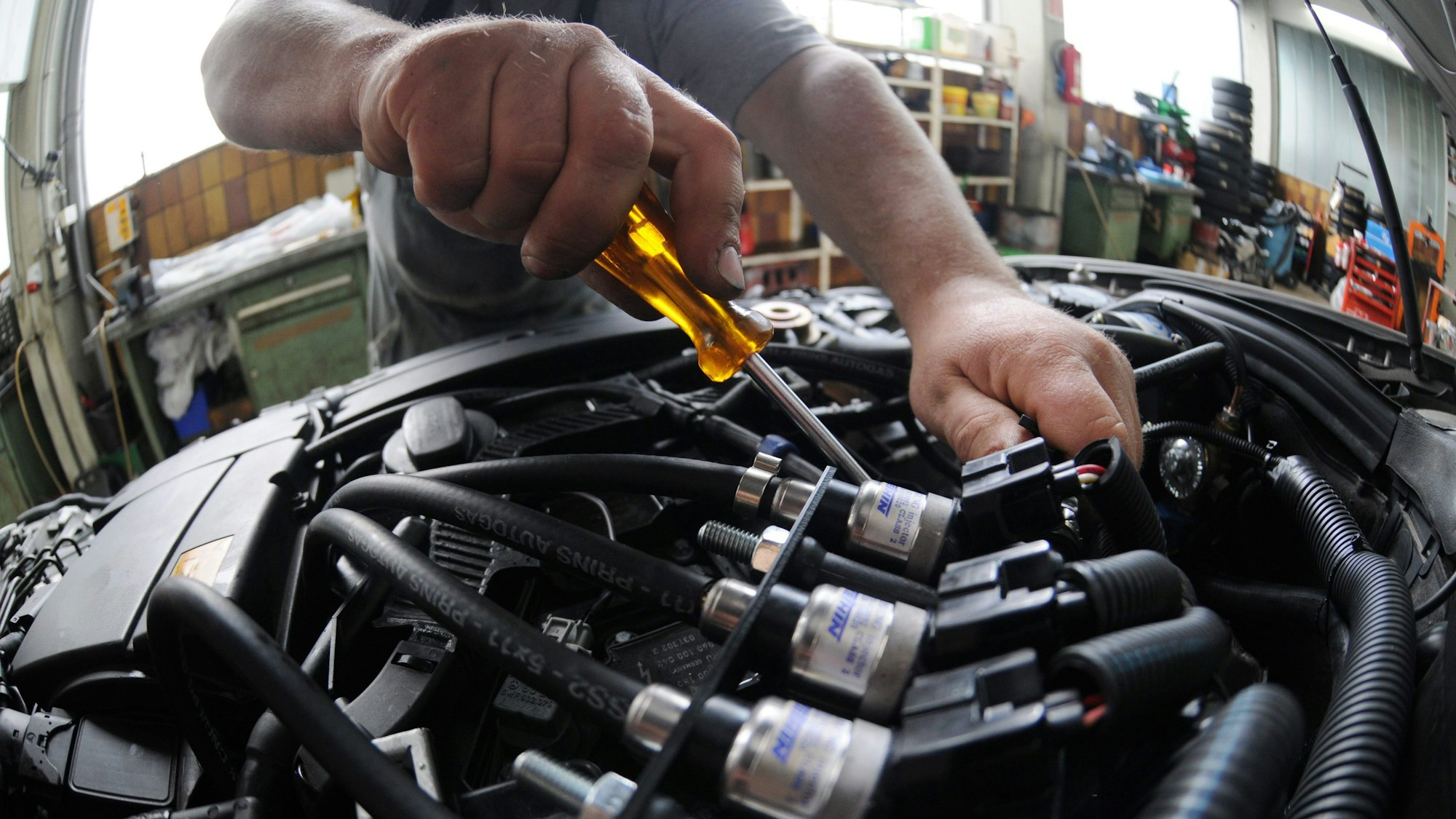 Ein Mechaniker arbeitet in einer Autowerkstatt im Motorraum eines Fahrzeugs mit Gasantrieb.