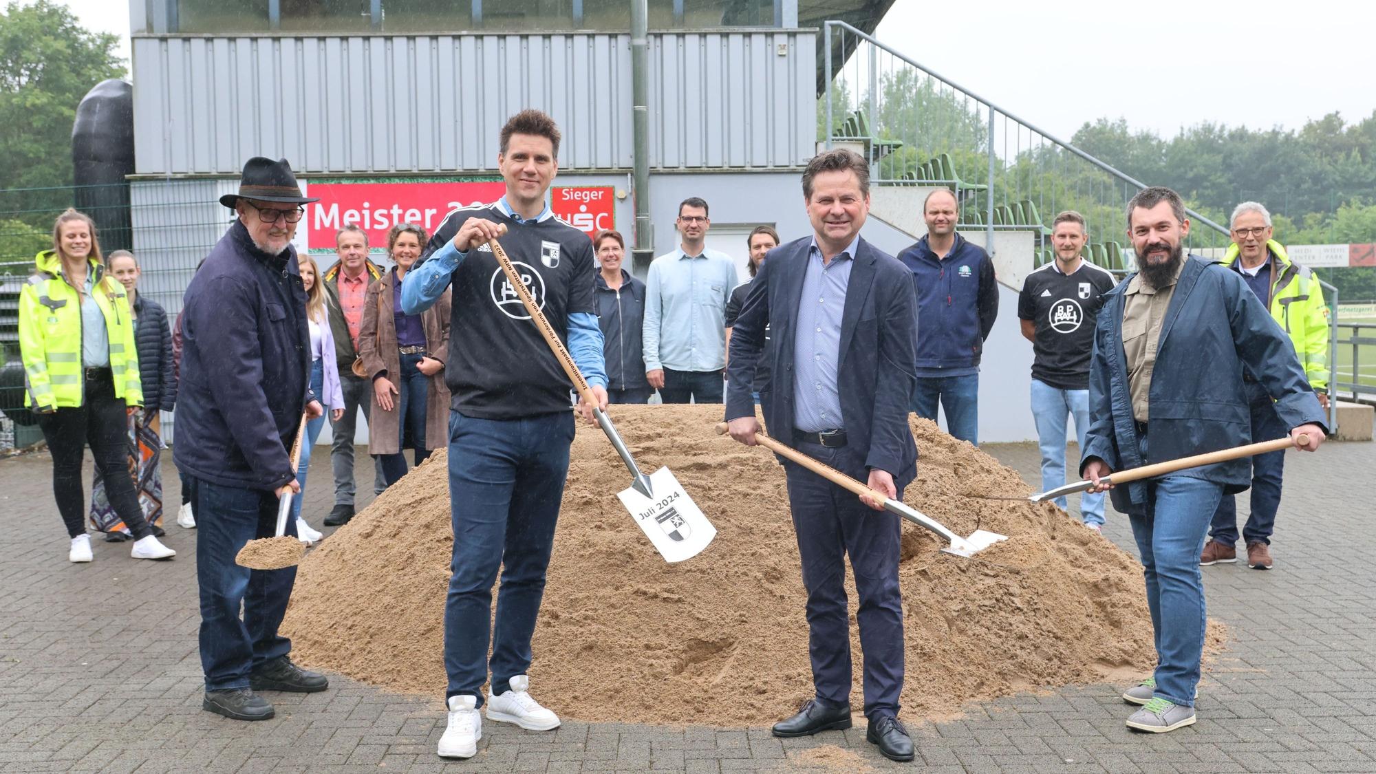 Vier Herren mit Spaten vor einem Sandhaufen.
