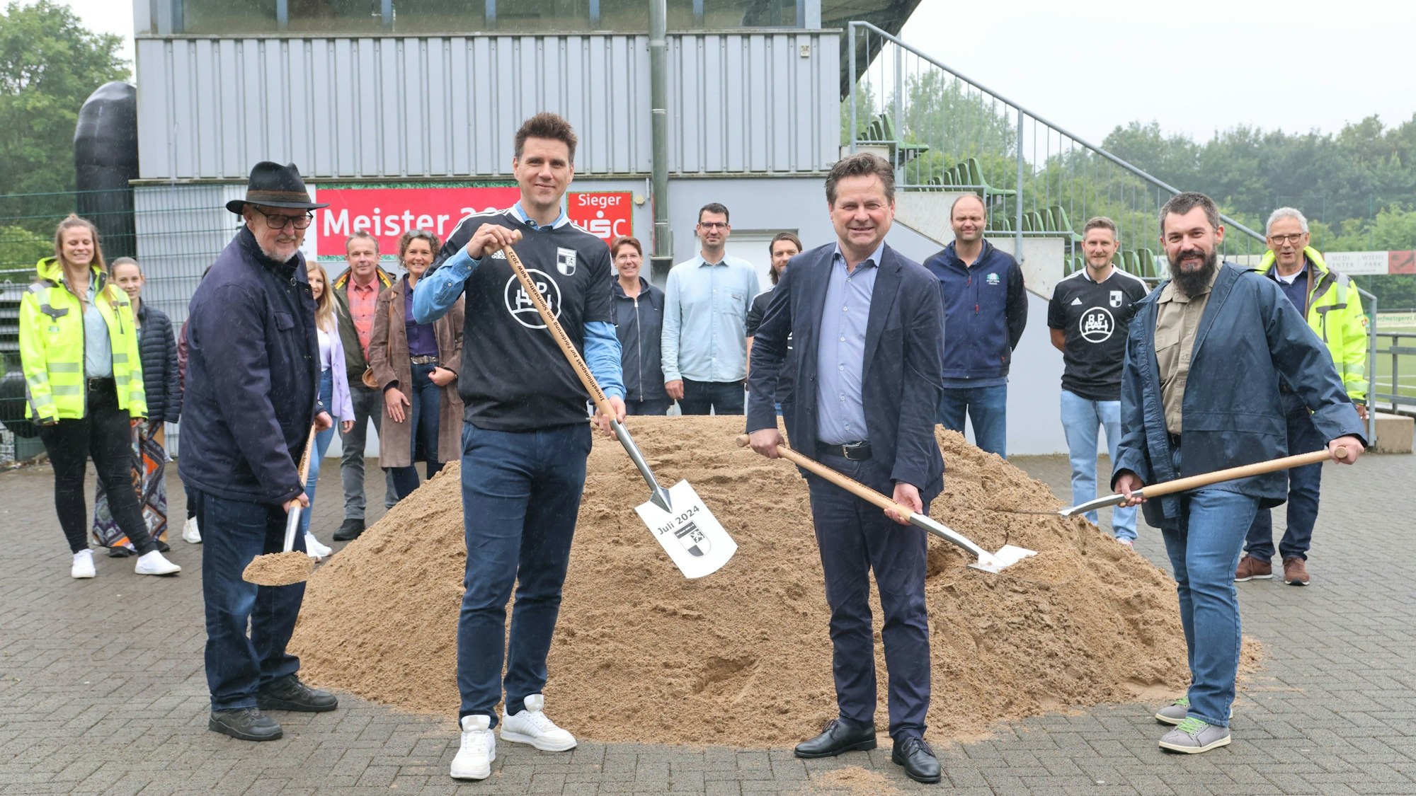 Vier Herren mit Spaten vor einem Sandhaufen.