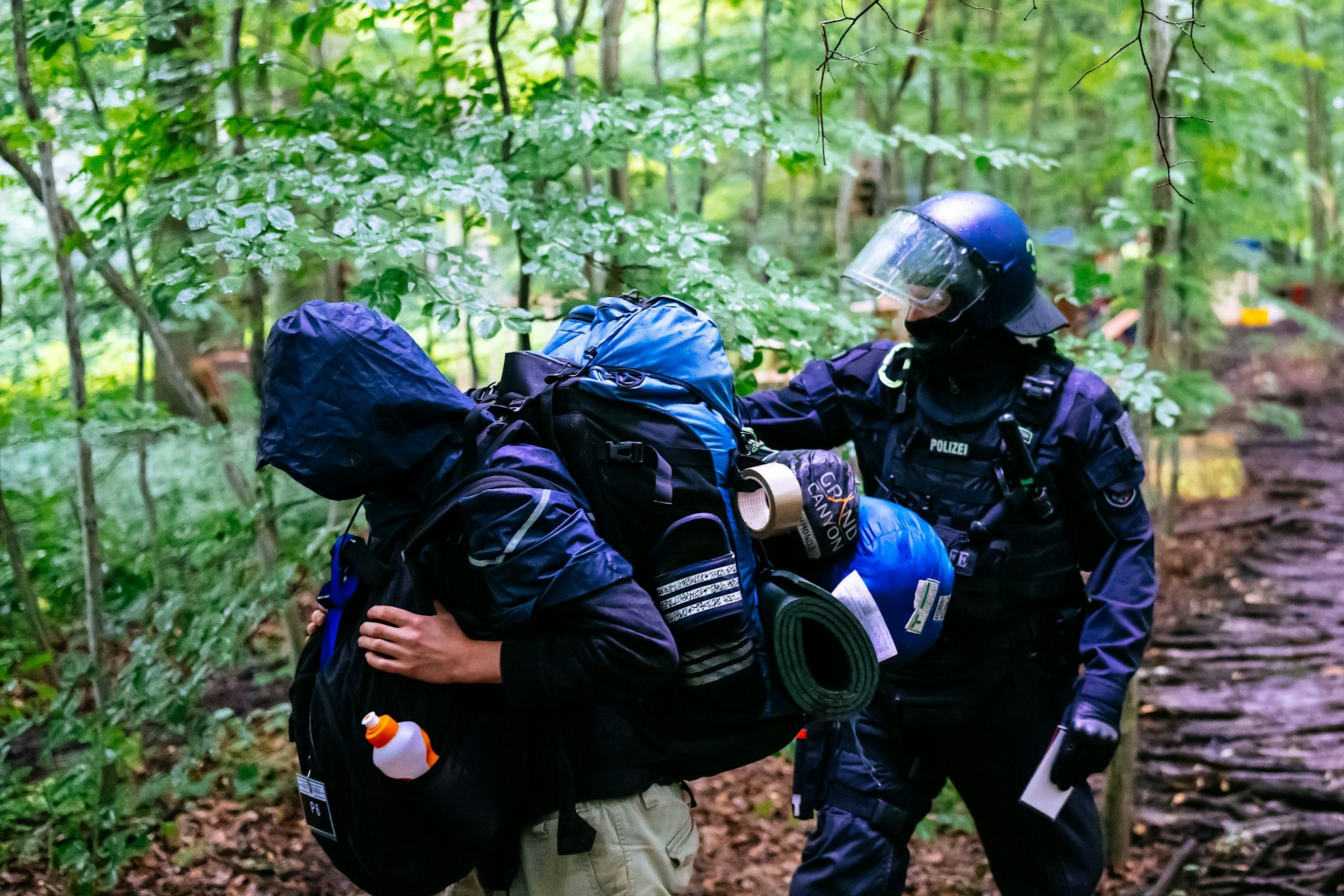 Ein Polizist weist einem Aktivisten den Weg aus dem Wald.