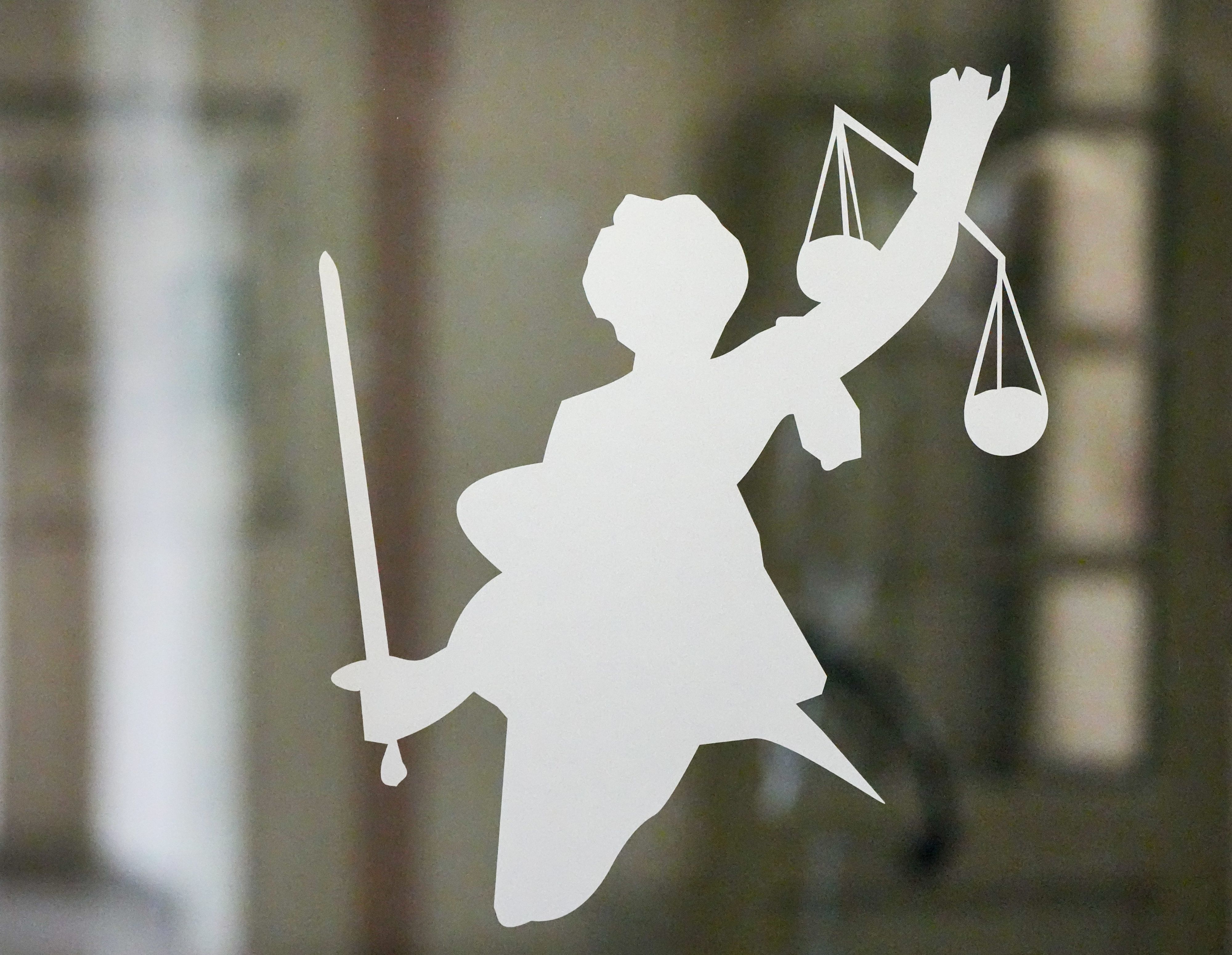 Die Figur der Justitia mit Richtschwert und Waage ist auf dem Glasfenster einer Tür im Gerichtsgebäude zu sehen.