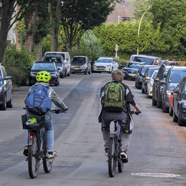 Zwei Radfahrer mit Schultaschen auf dem Rücken fahren nebeneinander auf der Bonnstraße in Hermülheim.