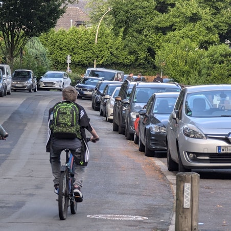 Zwei Radfahrer mit Schultaschen auf dem Rücken fahren nebeneinander auf der Bonnstraße in Hermülheim.