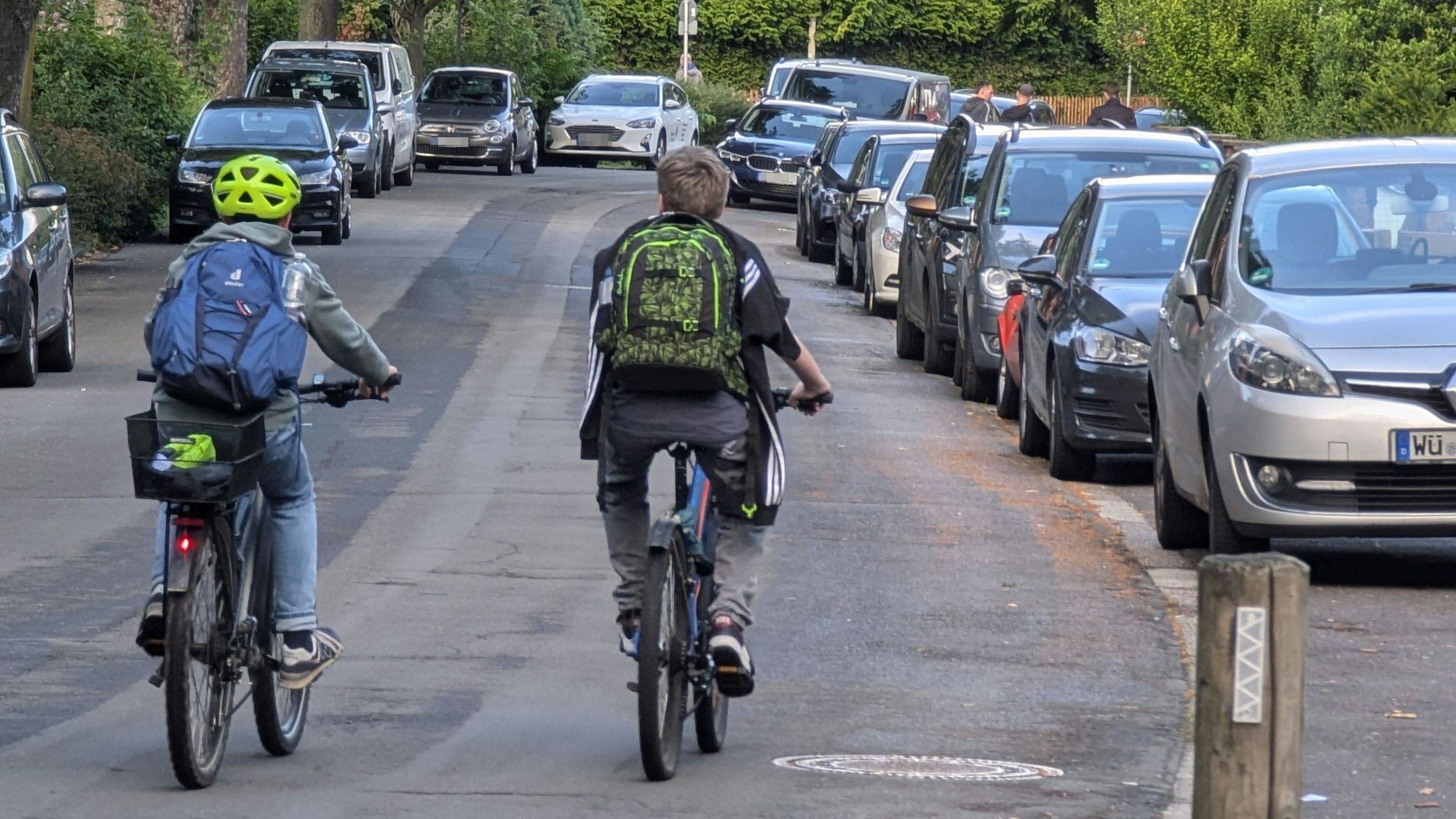 Zwei Radfahrer mit Schultaschen auf dem Rücken fahren nebeneinander auf der Bonnstraße in Hermülheim.