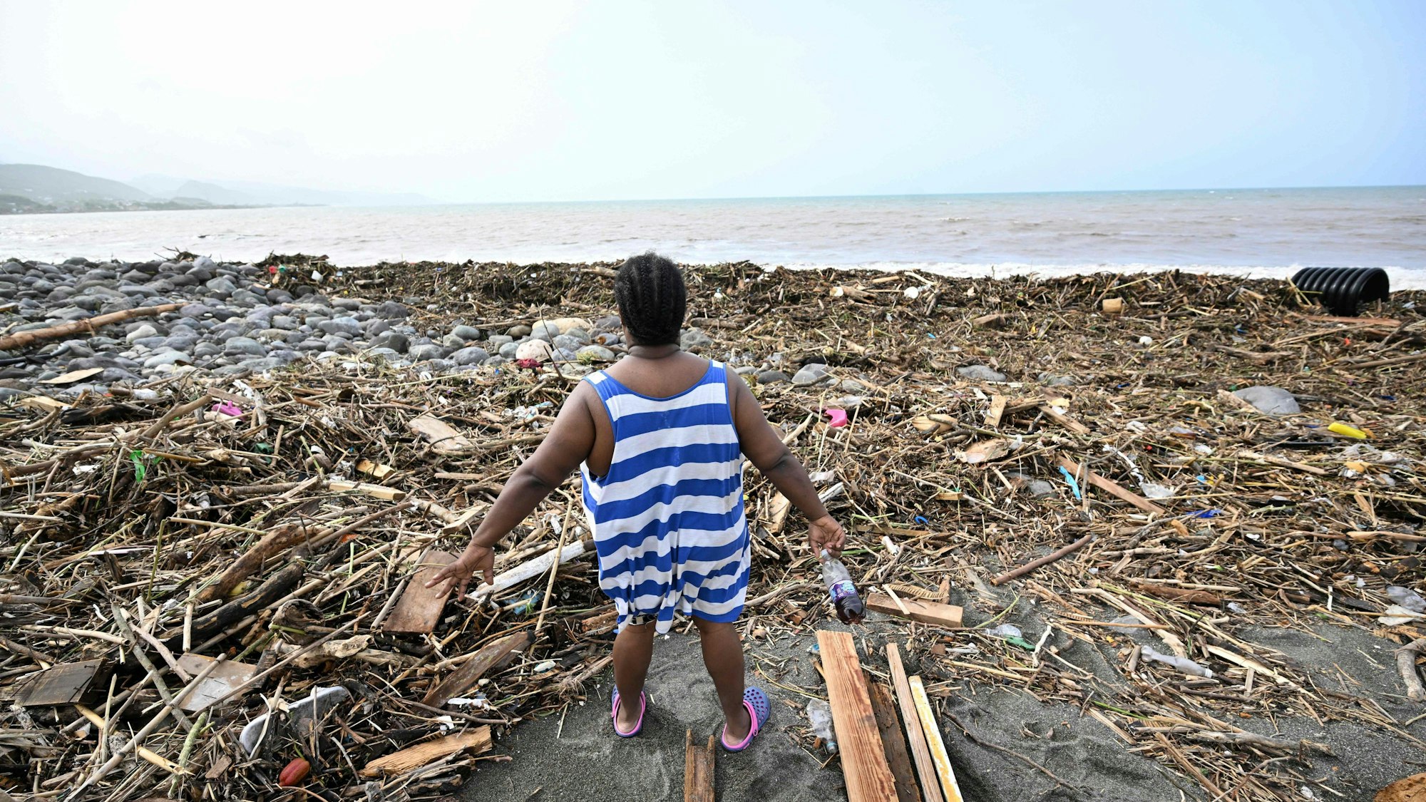 Eine Frau steht am Strand in Holzstücken und Müll.