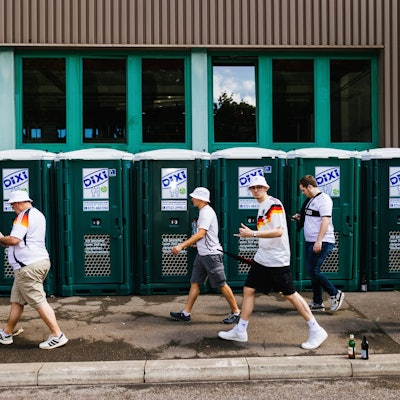 Deutsche Fans gehen beim Fanmarsch in der Innenstadt an mobilen Toiletten vorbei.