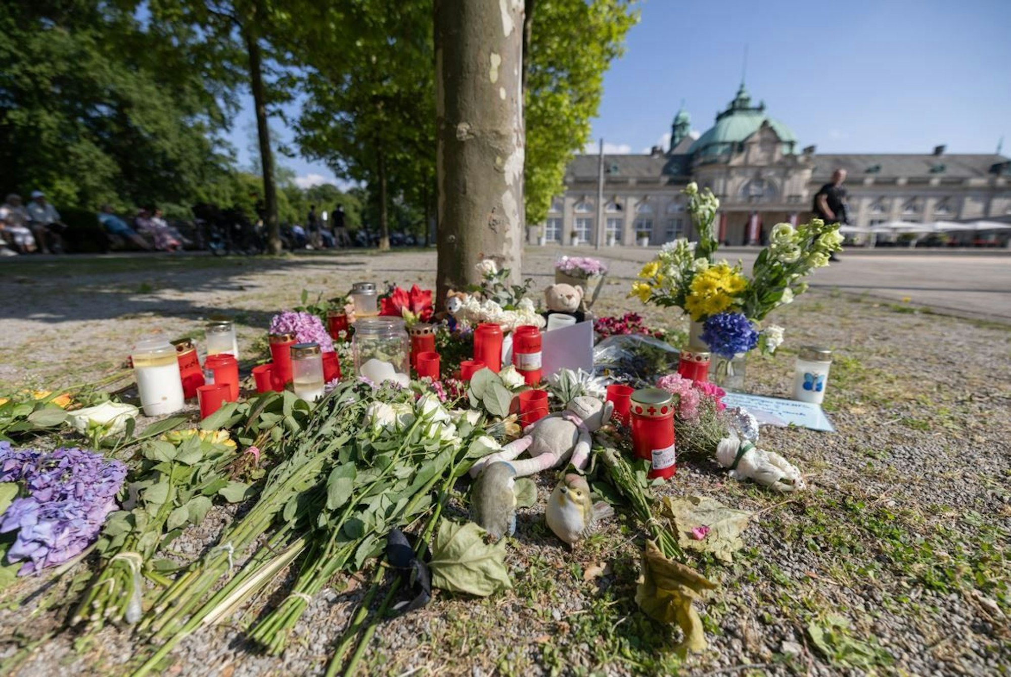 Blumen, Kerzen und handgeschriebene Trauerbekundungen stehen an einem Baum im Kurpark Bad Oeynhausen.