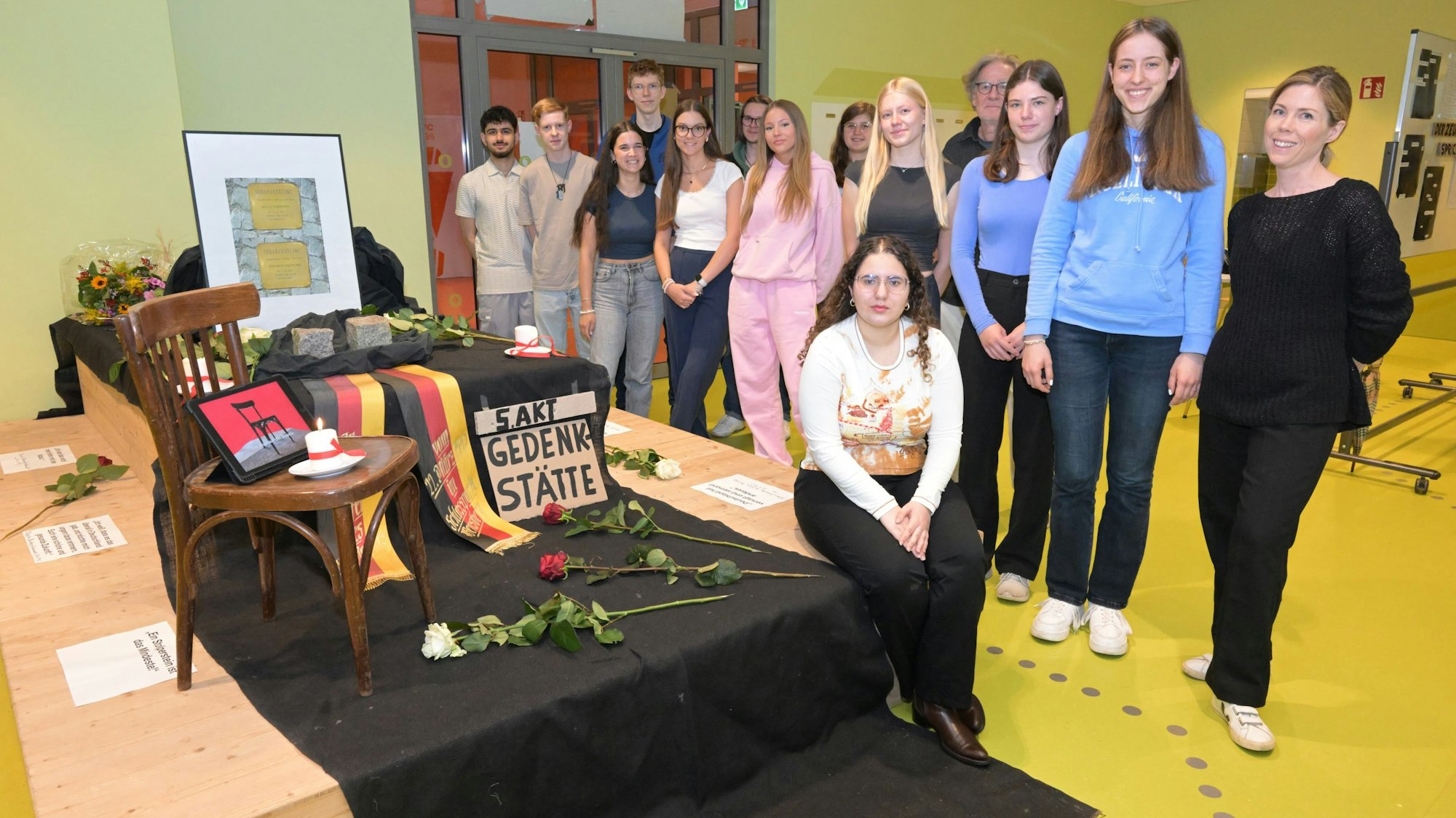 Schülerinnen und Schüler stehen neben dem Mahnmal, das sie in einem Klassenraum aufgebaut haben.