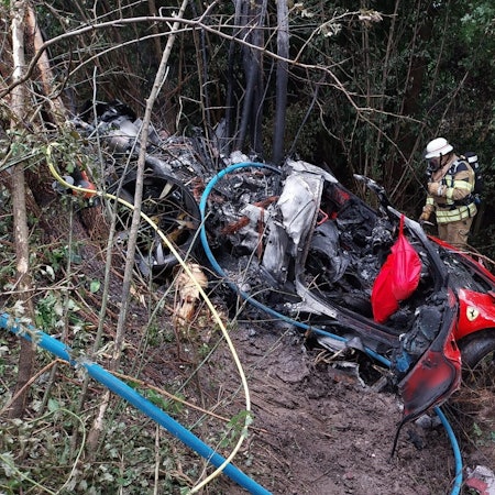 Feuerwehrleute stehen neben einem ausgebrannten Sportwagen.