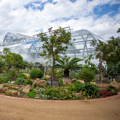 Auch von außen schön: Die Schaugewächshäuser mit umgebender Bepflanzung. Blumenrabatten und halbhohe Büsche zwischen Natursteinen schmücken die Umgebung