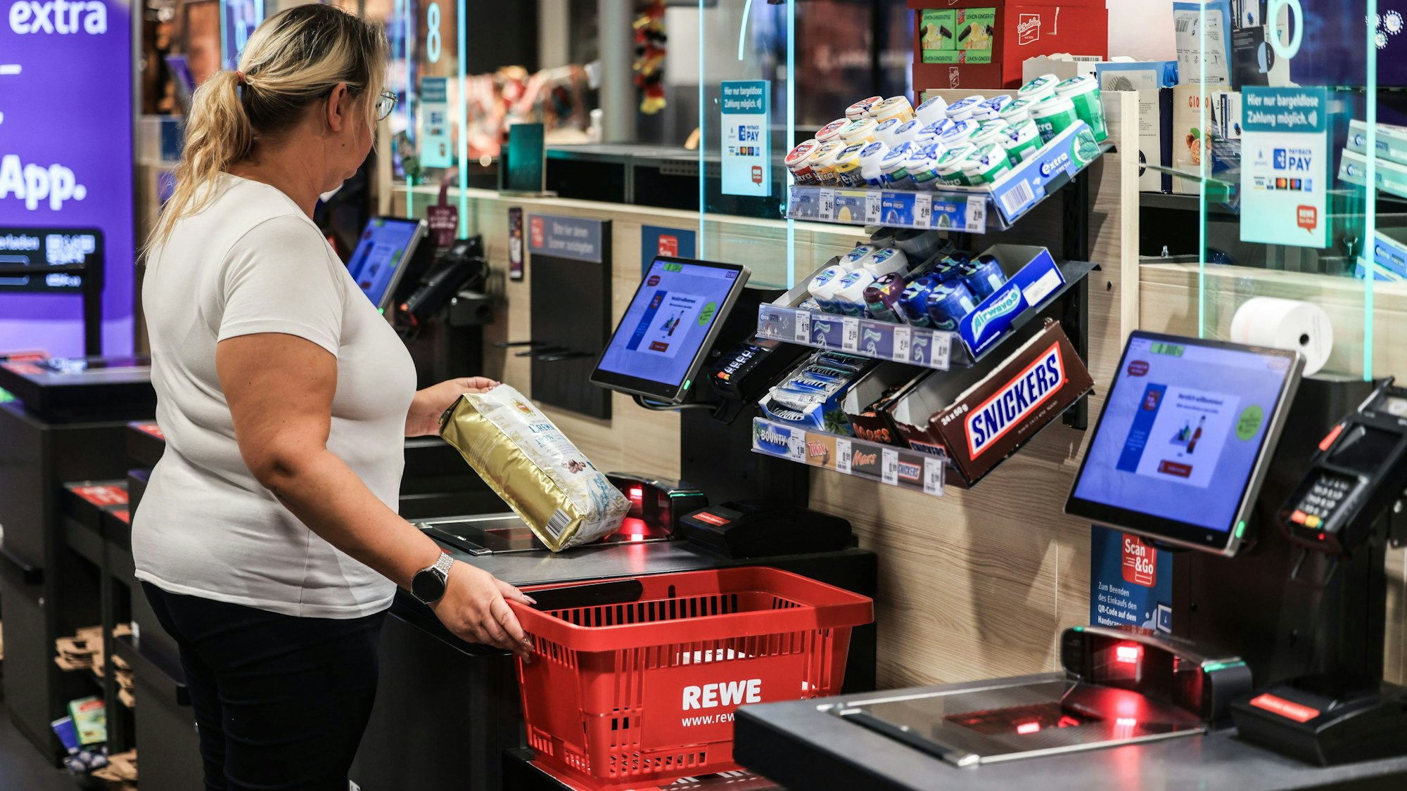 Eine Frau scannt in einer Rewe-Filiale ein Produkt an einer Selbstbedienungskasse.