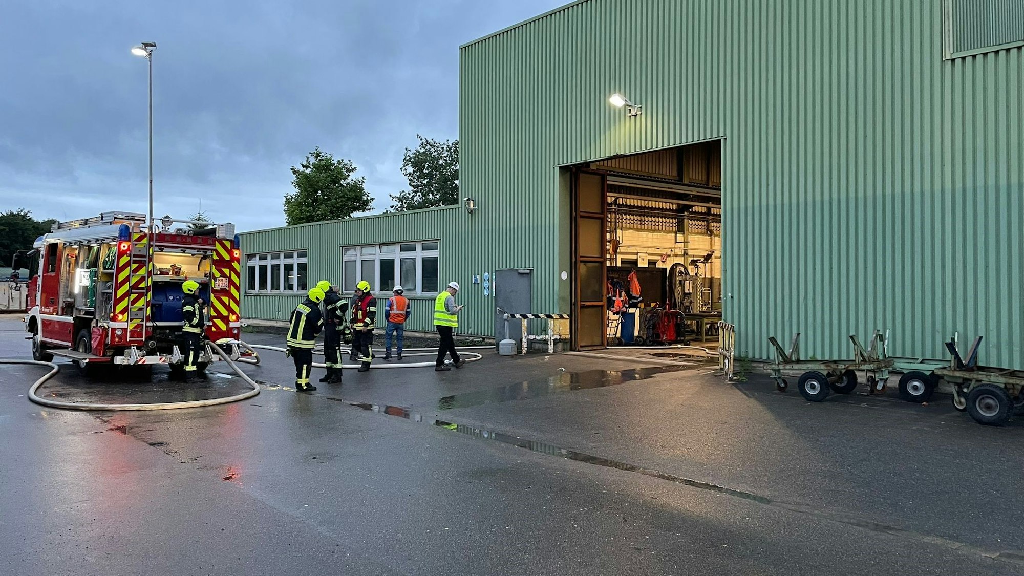 Einsatzkräfte der Feuerwehr vor der verrauchten Industriehalle.