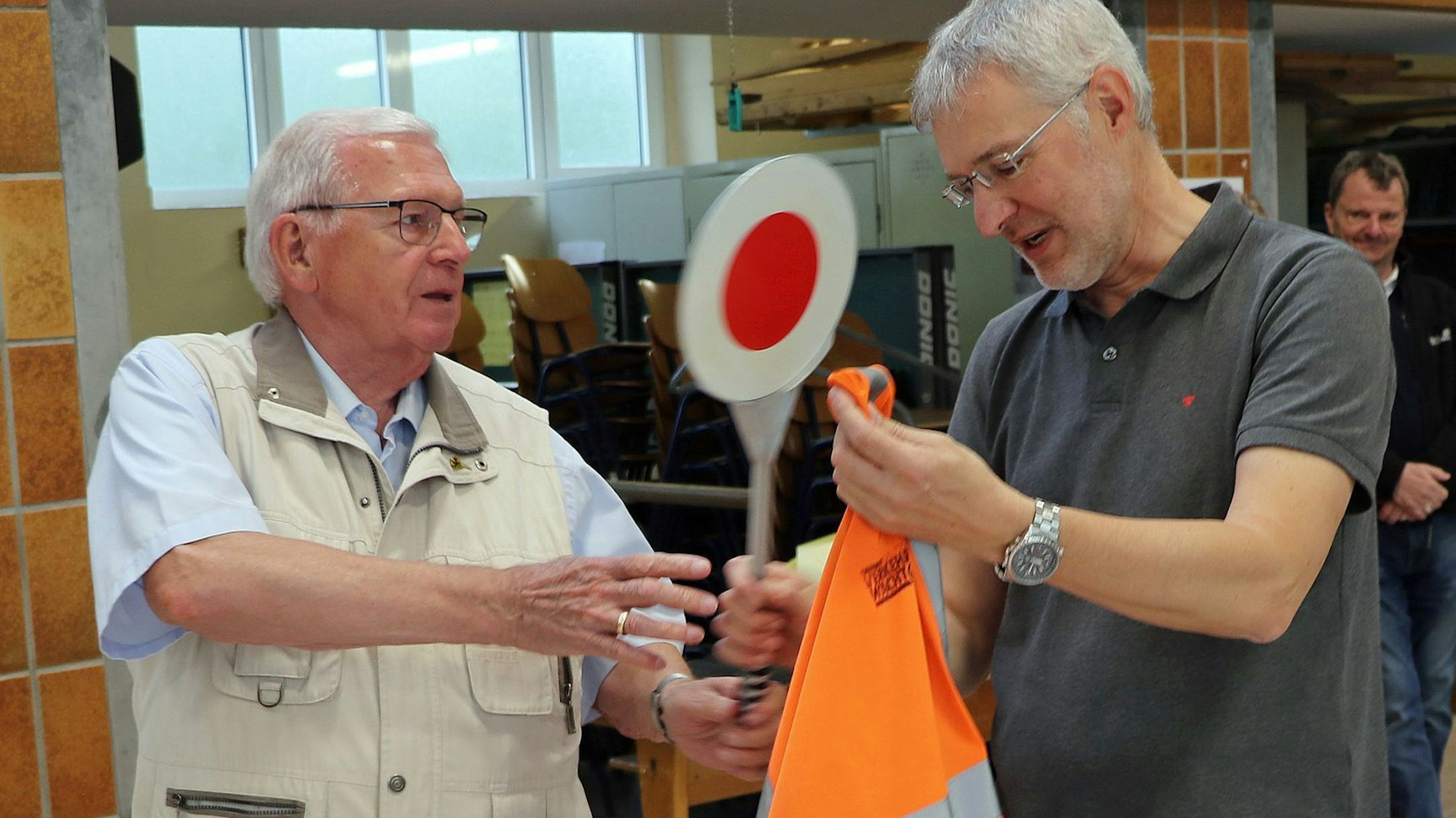 Auf dem Bild ist zu sehen, wie Franz Becker die Warnkelle und -weste an den Schulleiter zurück gibt